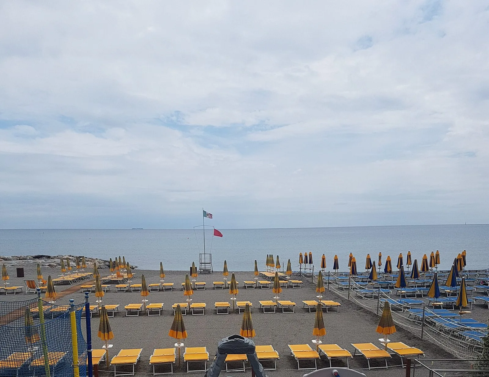 Spiaggia di Loano con lettini gialli, ombrelloni chiusi e mare calmo sotto un cielo nuvoloso