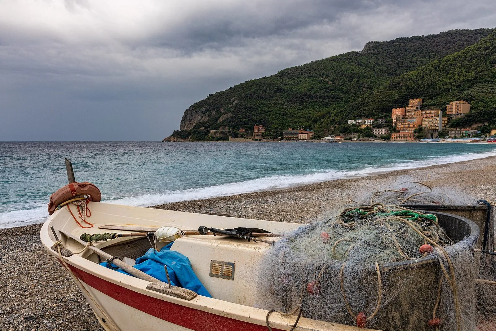 Barca da pesca con le reti tirata in secco sulla spiaggia di Noli, con il golfo e il promontorio sullo sfondo